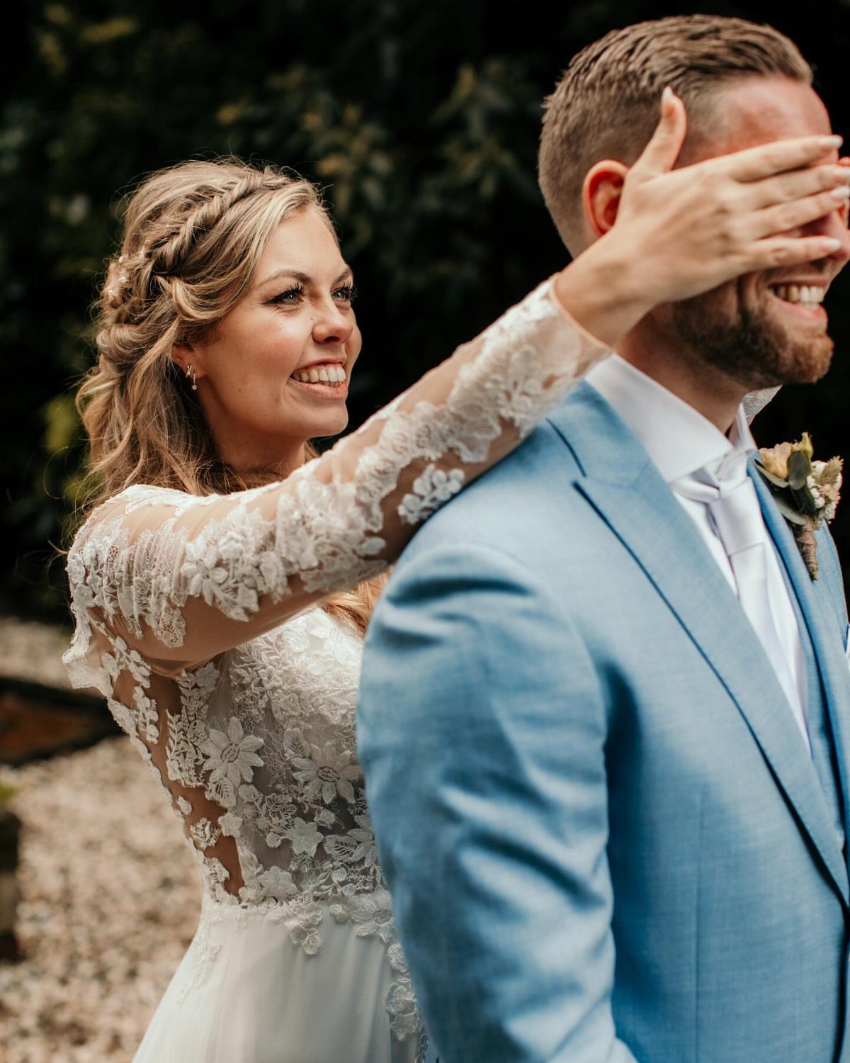 Bride in lace dress covering the groom's eyes during a first look moment.