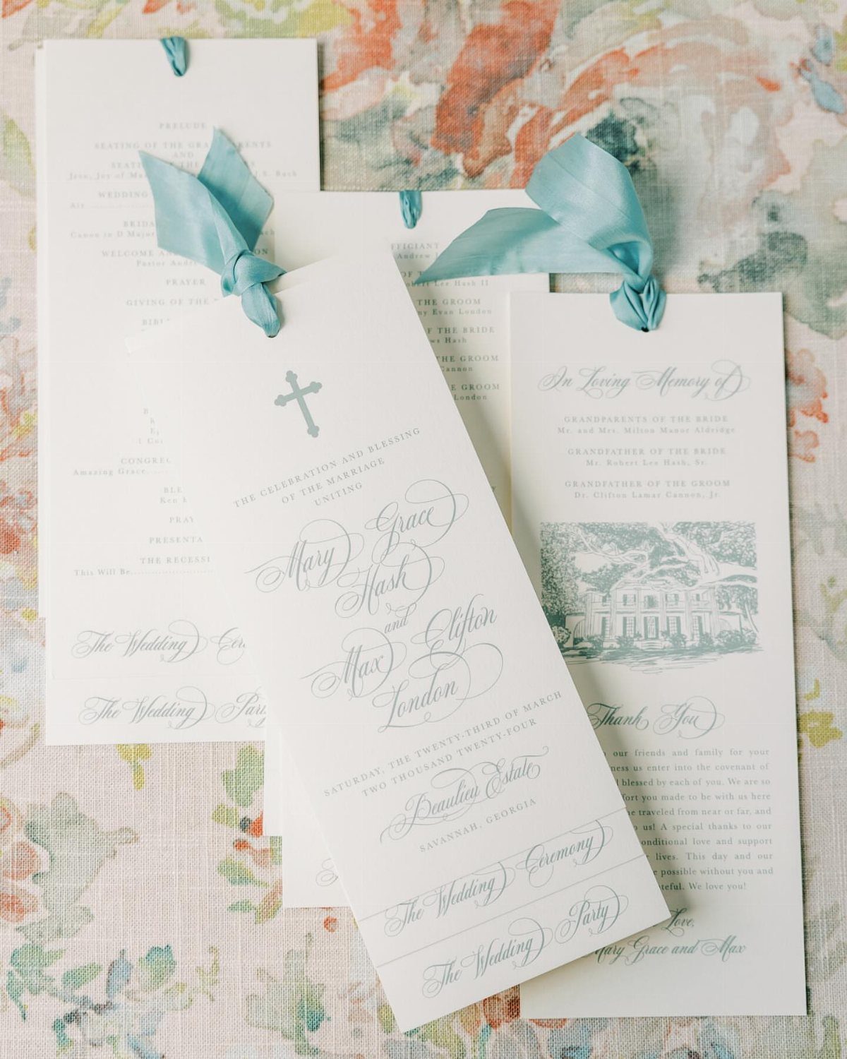 Wedding programs with cursive calligraphy and blue ribbons on floral fabric background