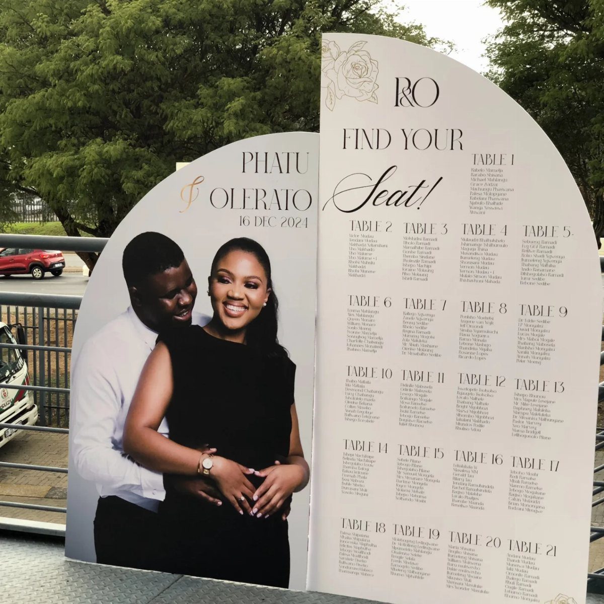 Arched wedding seating chart with a couple's photo and guest table assignments.