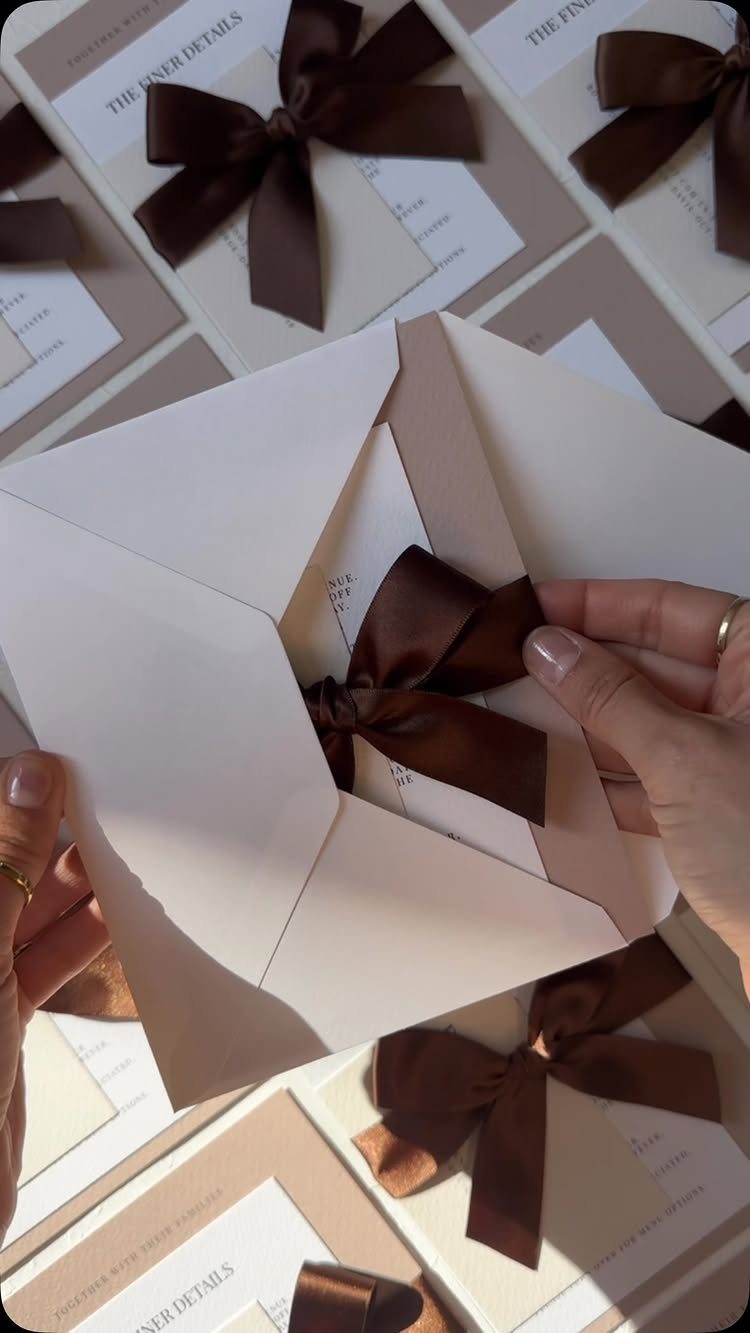 Wedding invitation samples with brown satin bows and white envelopes on a table