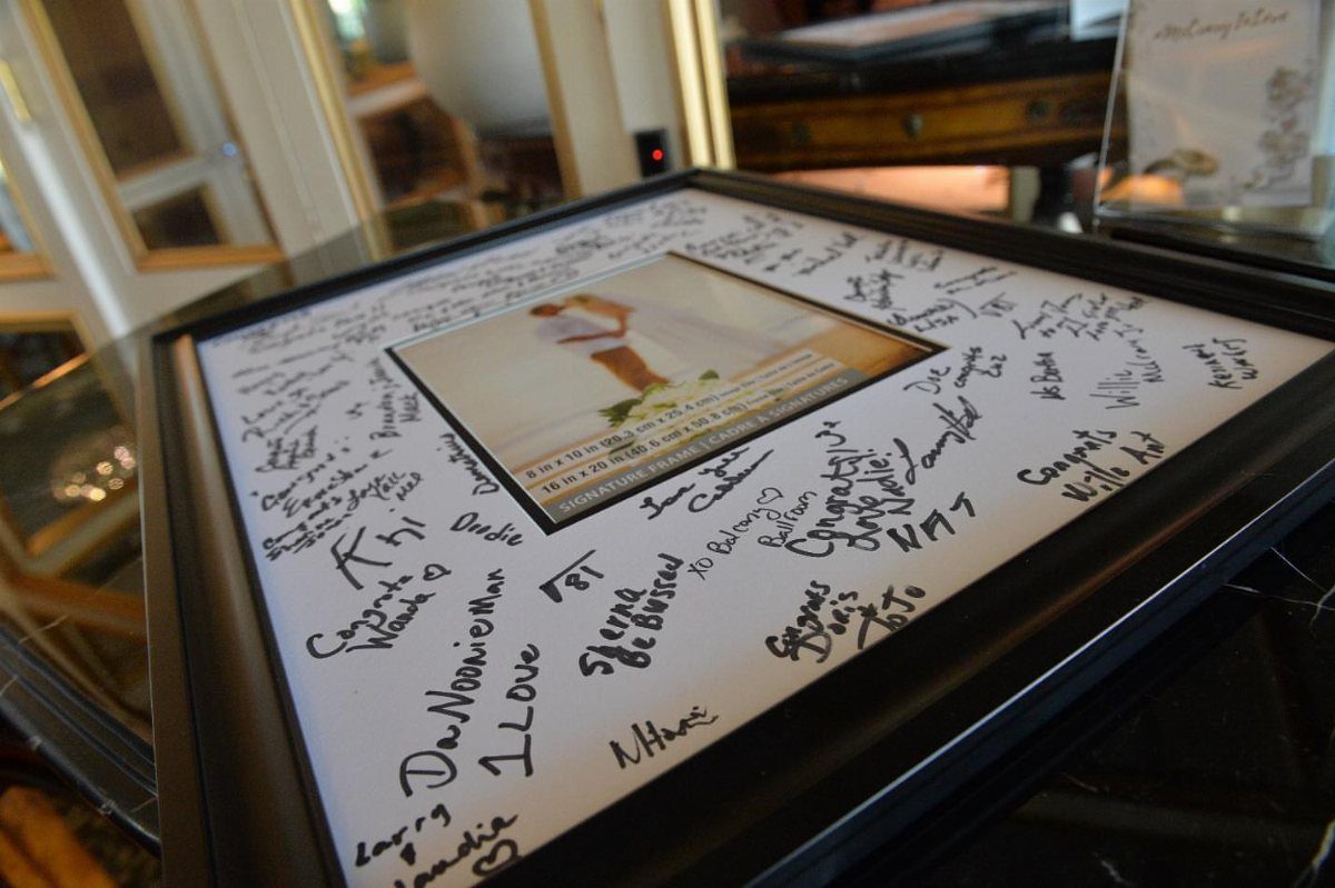 Black picture frame with a central photo and handwritten guest signatures on the mat.