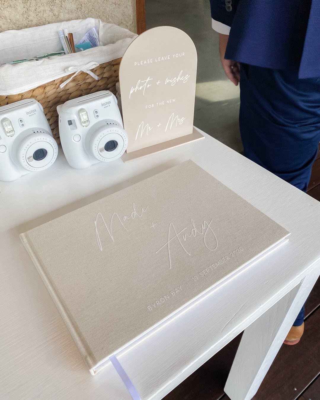 Two white instant cameras and a beige guest book on a white table.