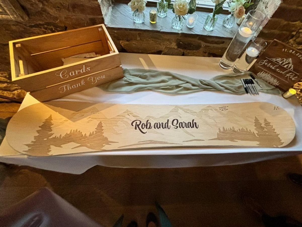 Wooden snowboard guest book with engraved names and mountains on a white table