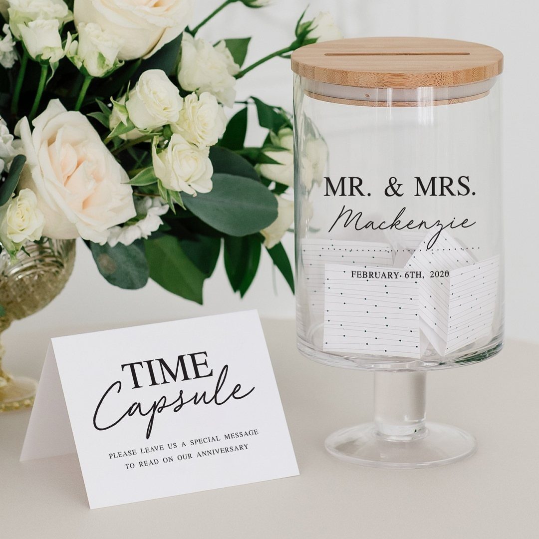 Glass time capsule jar with wooden lid and notes next to white roses