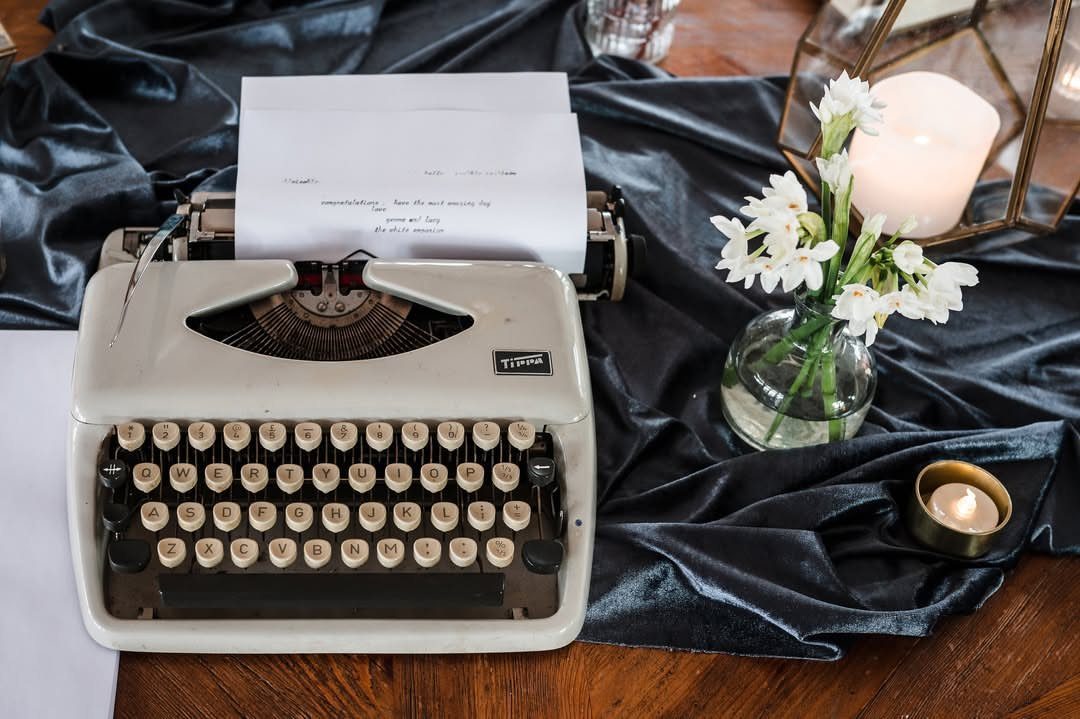 Vintage cream typewriter with paper, white flowers, and candles on blue velvet fabric.