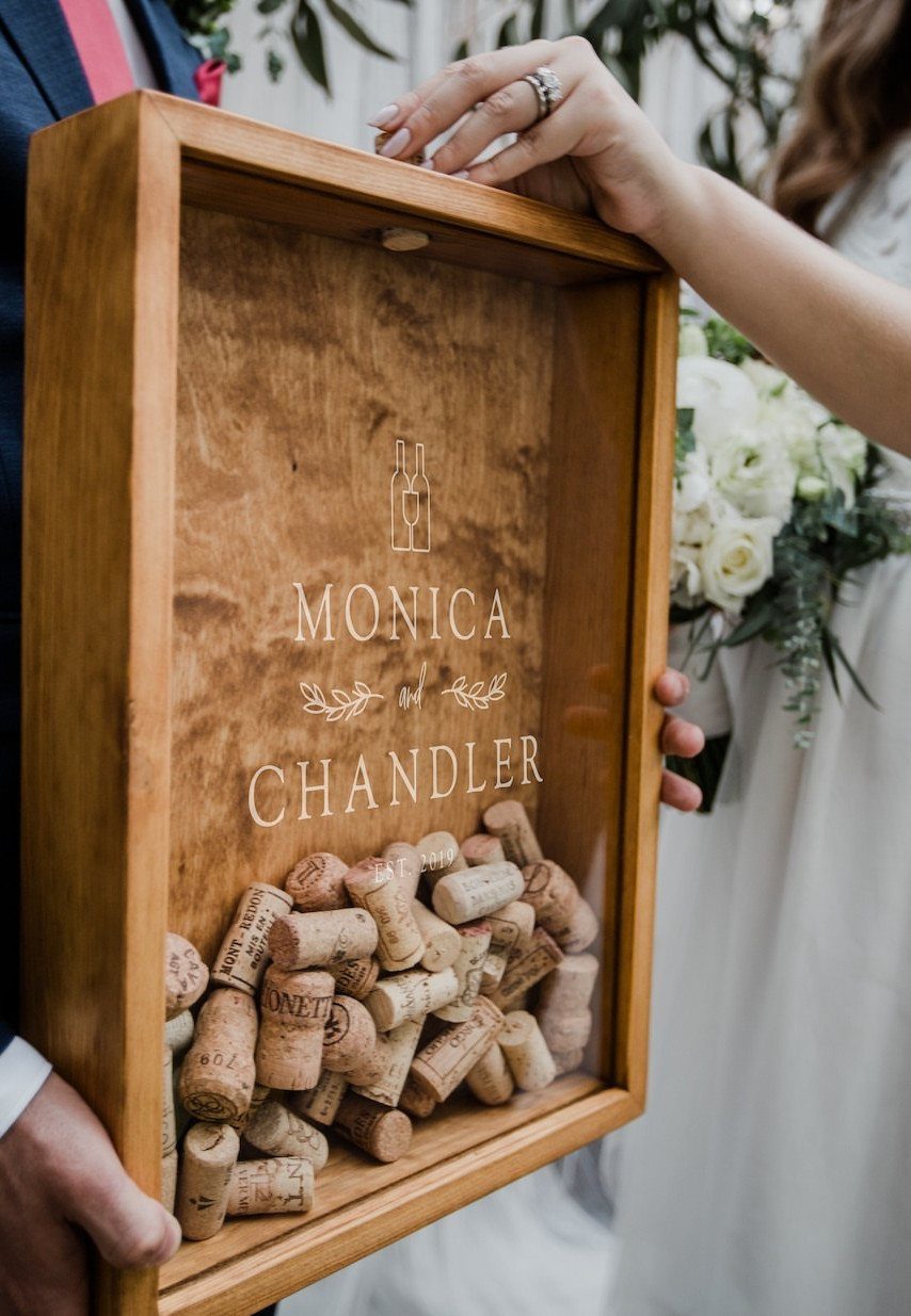 Wooden shadow box filled with wine corks and engraved names held by couple