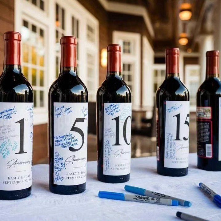 Wine bottles with anniversary year labels signed by guests on a white table.