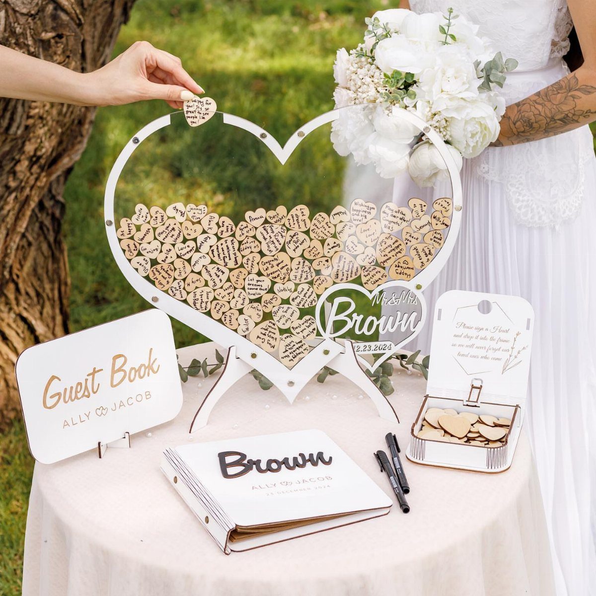 Heart-shaped acrylic guest book filled with small wooden heart tokens on a table.