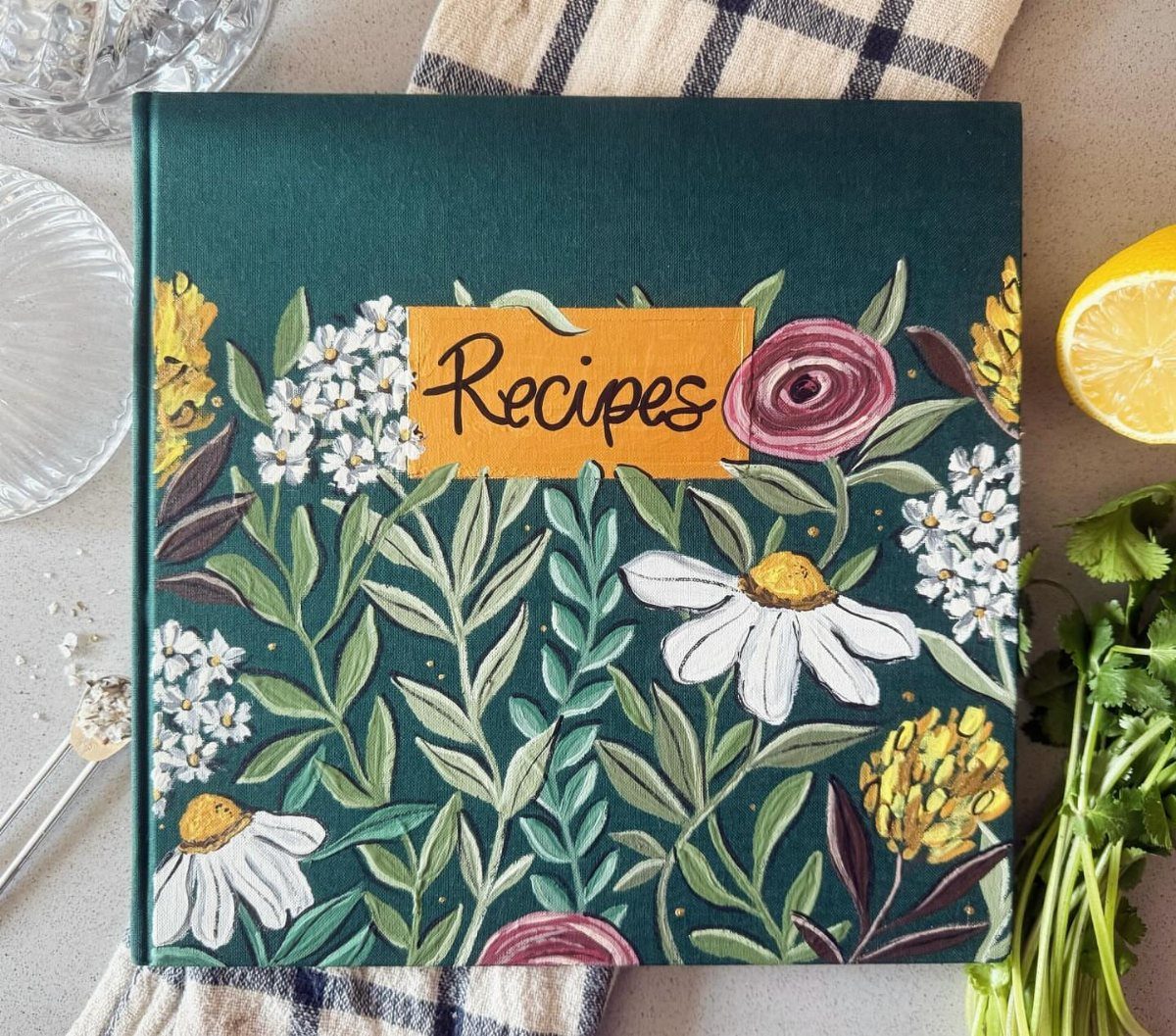 Green recipe book with floral cover and yellow label next to fresh ingredients.