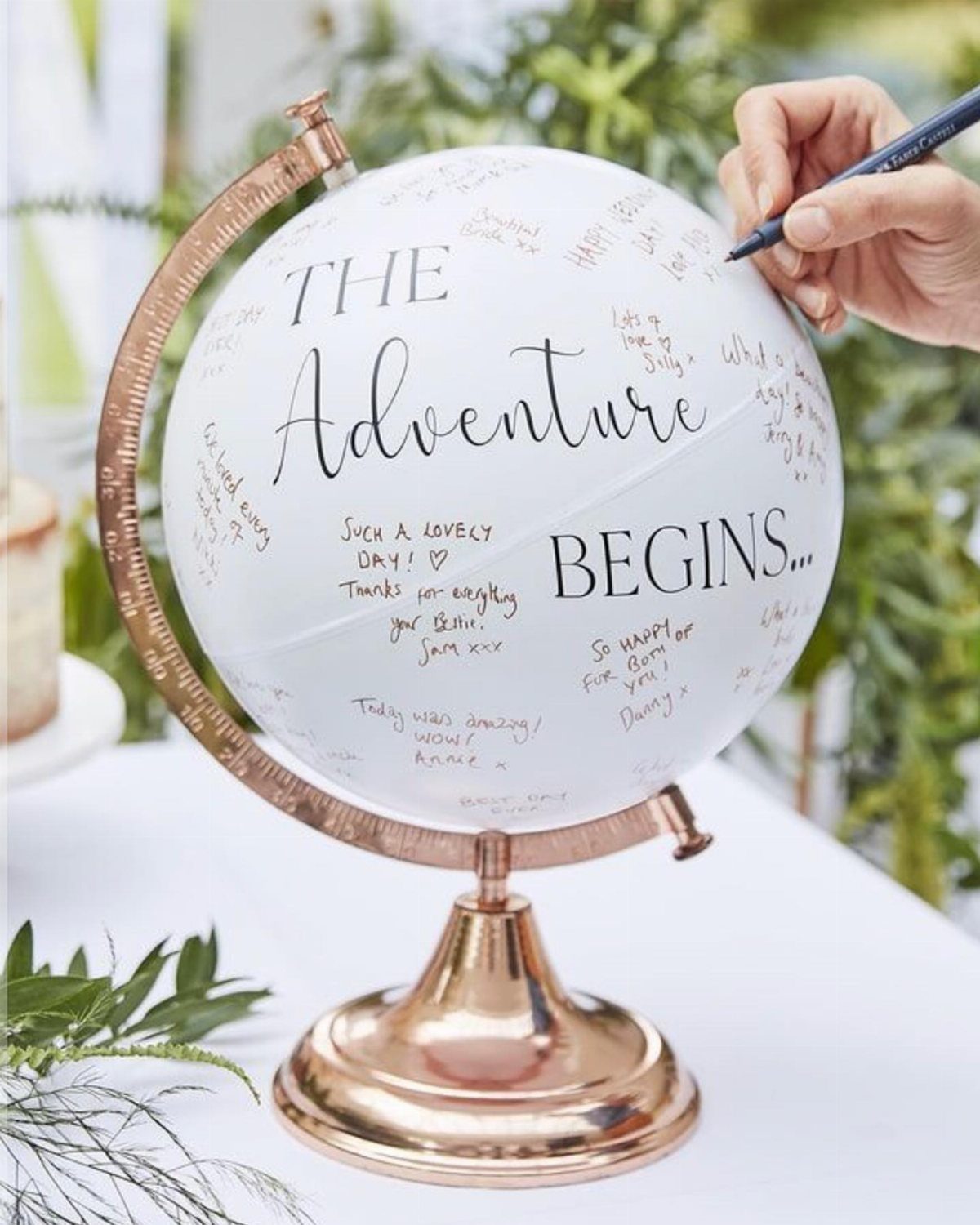 White globe with rose gold stand being signed with handwritten messages and text.