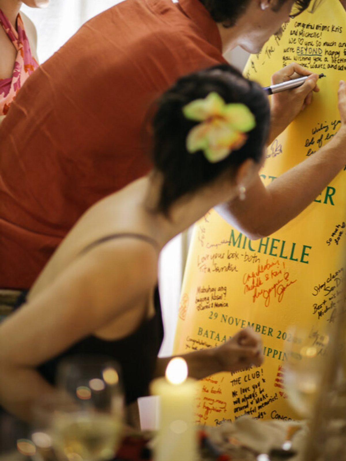 Guests signing a yellow surfboard with handwritten messages at a celebratory event.