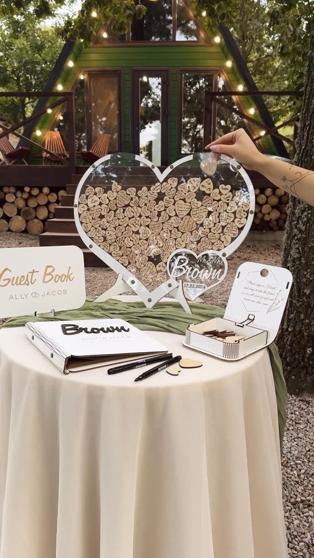 Heart-shaped acrylic box filled with wooden heart tokens on a wedding guest book table