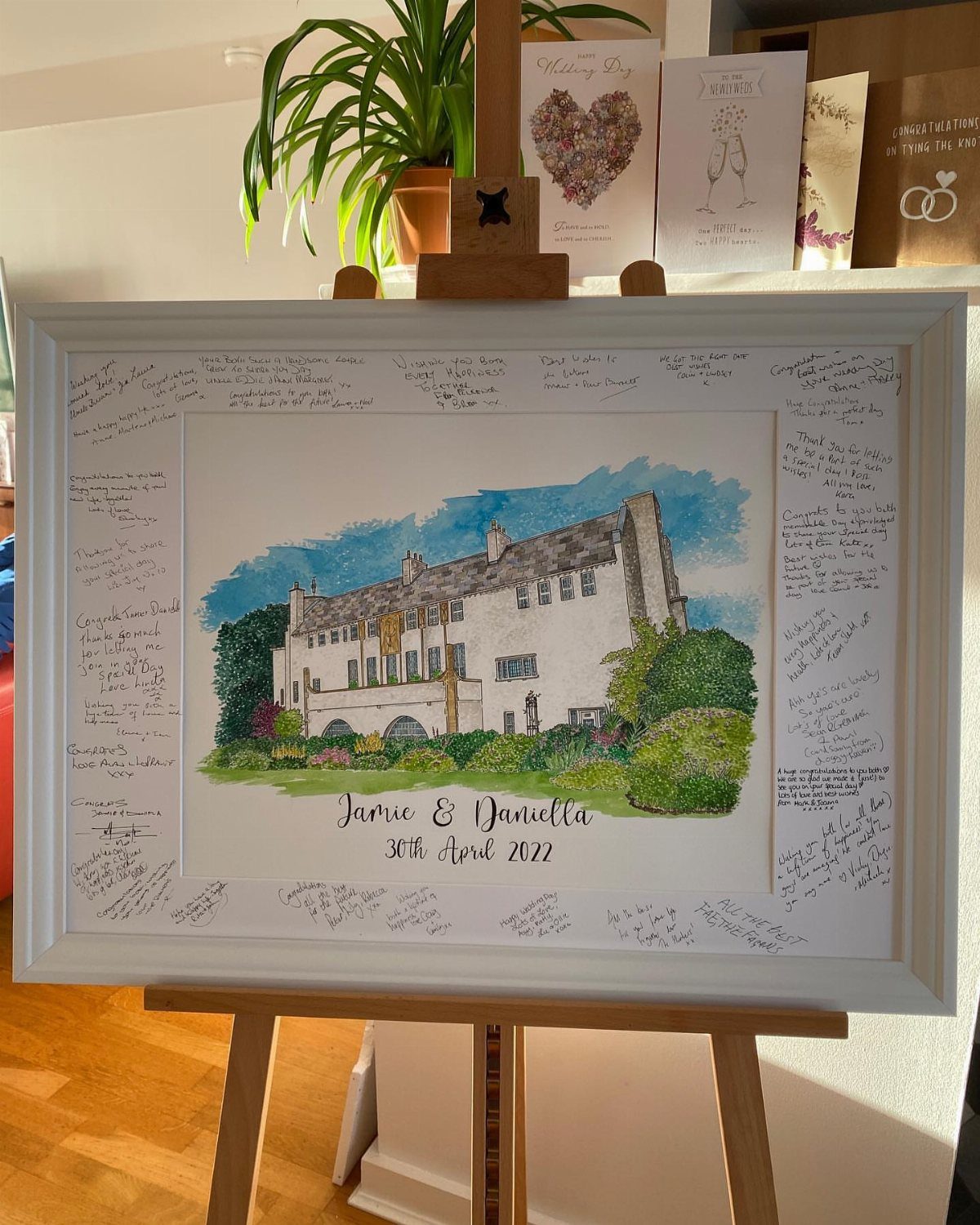 Watercolor painting of a venue in a white frame signed by wedding guests.