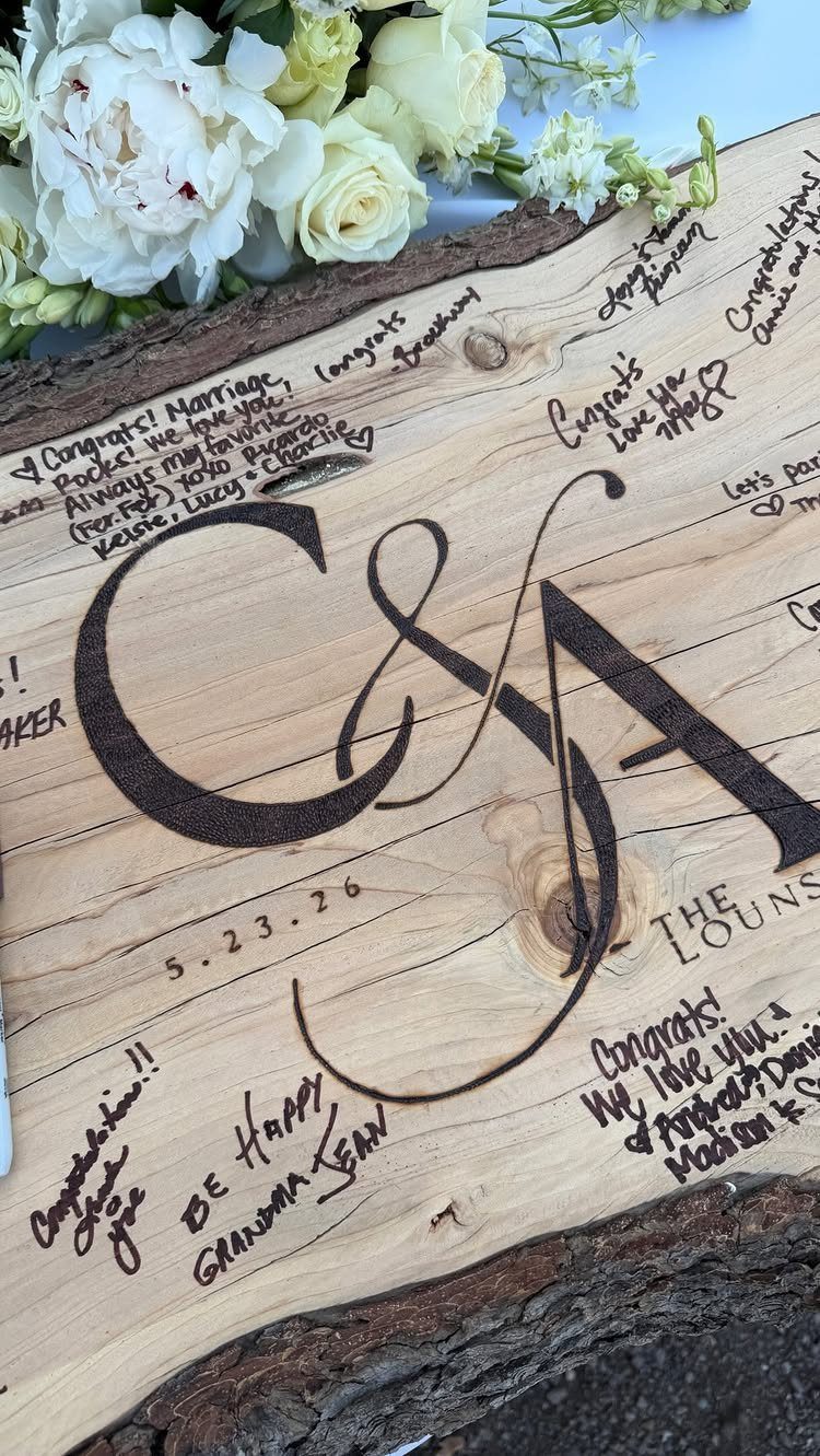 Wooden slice guest book with calligraphic initials and handwritten guest messages and signatures.