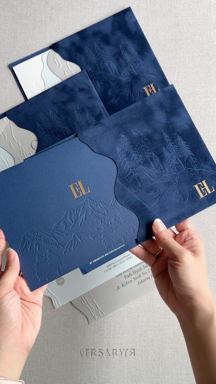 Navy blue wedding invitations with gold foil initials and embossed mountain details.