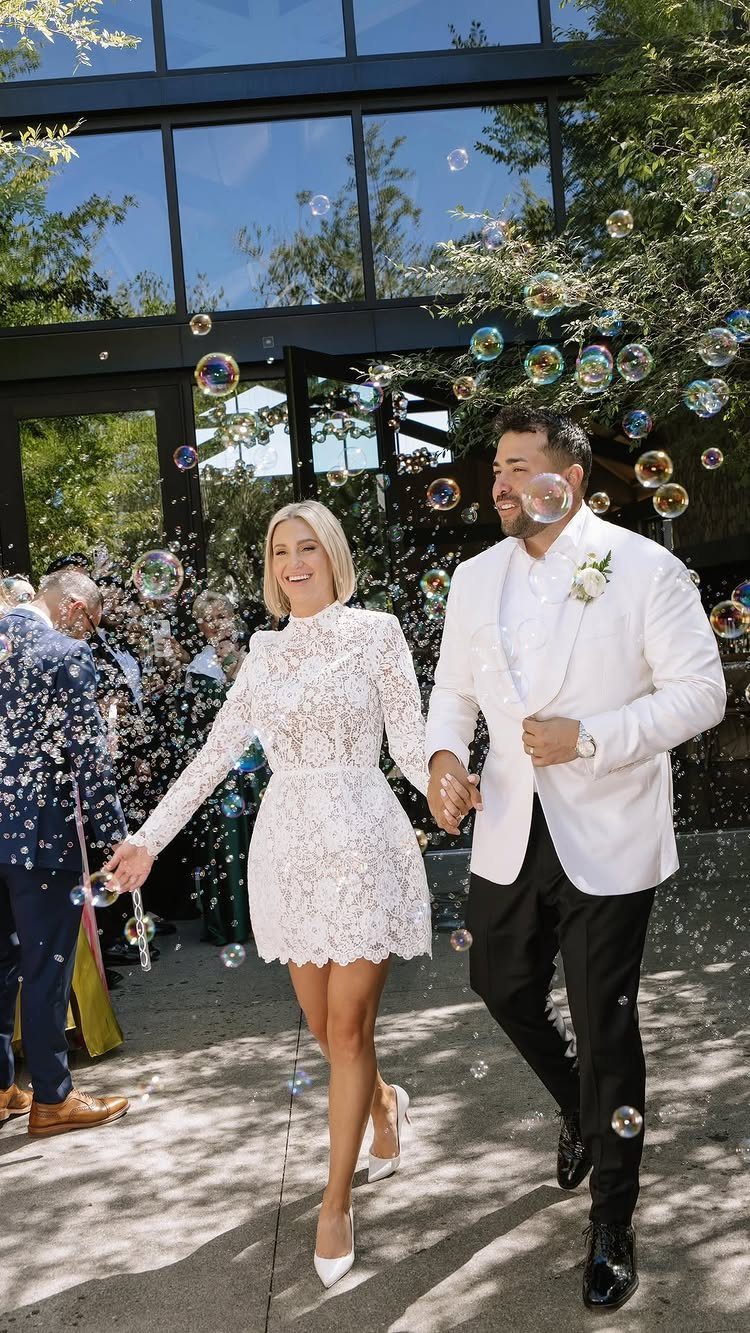 Bride and groom walking through bubbles in front of a modern glass building.