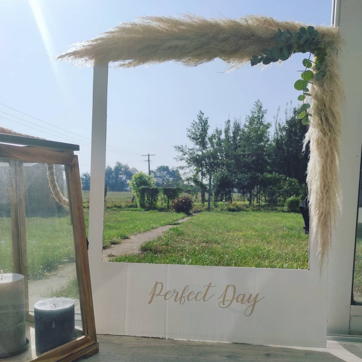 White decorative frame with pampas grass and gold text in a grassy field
