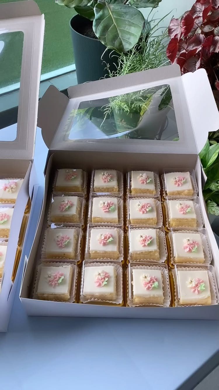 Small square white cakes with floral toppings in a white cardboard delivery box.