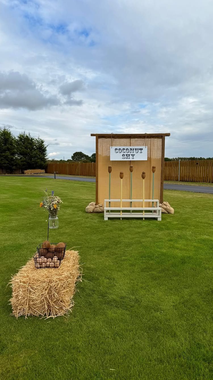 Coconut Shy game booth and hay bale with flowers on a green lawn