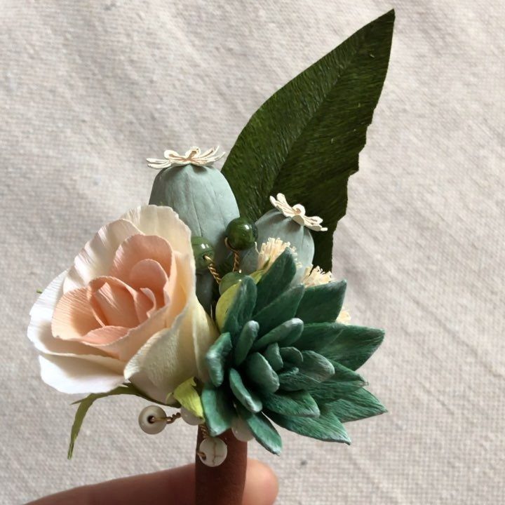 Boutonniere with a peach paper rose, green succulent, and blue-grey seed pods.