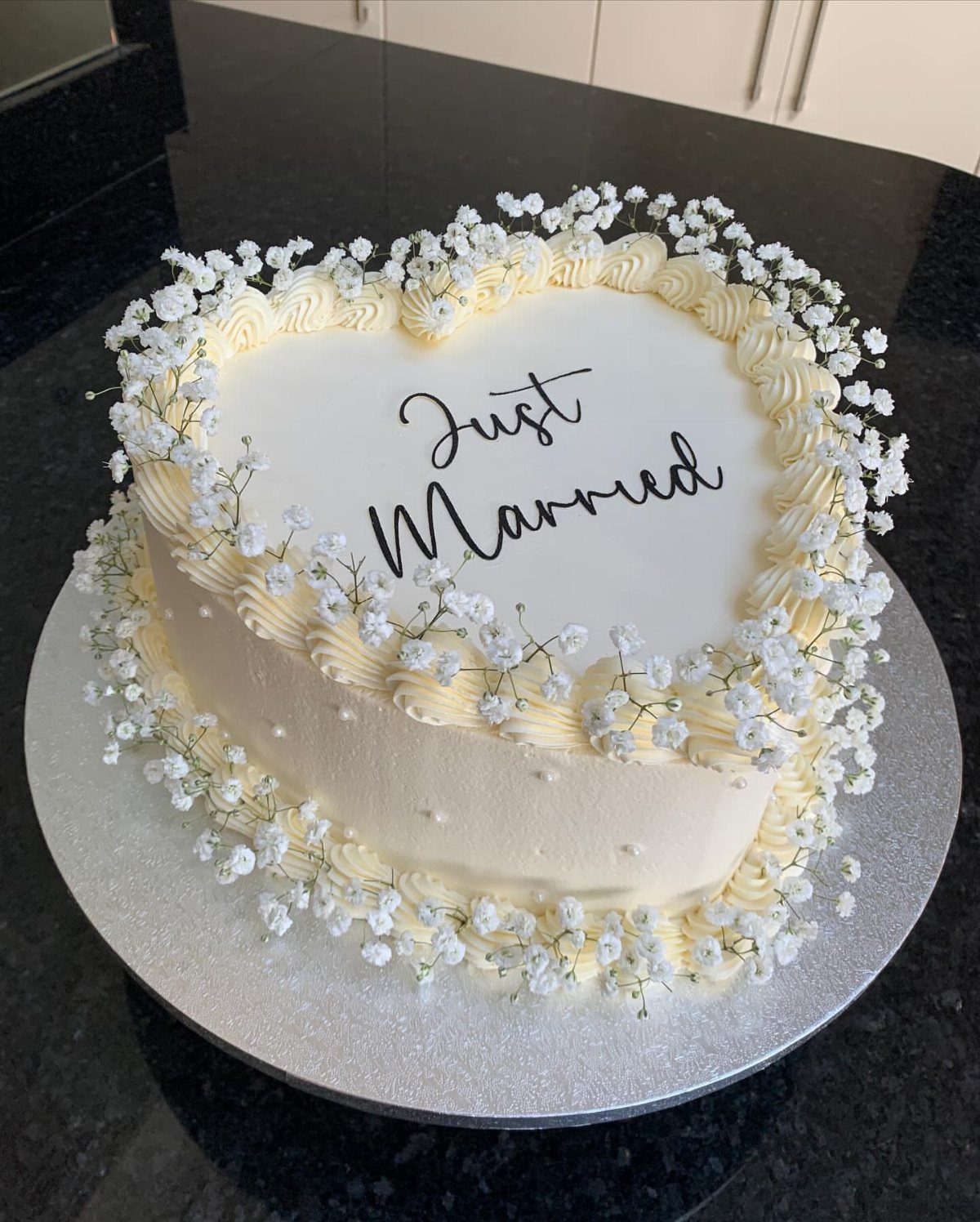 Heart-shaped white wedding cake decorated with baby's breath and Just Married text.