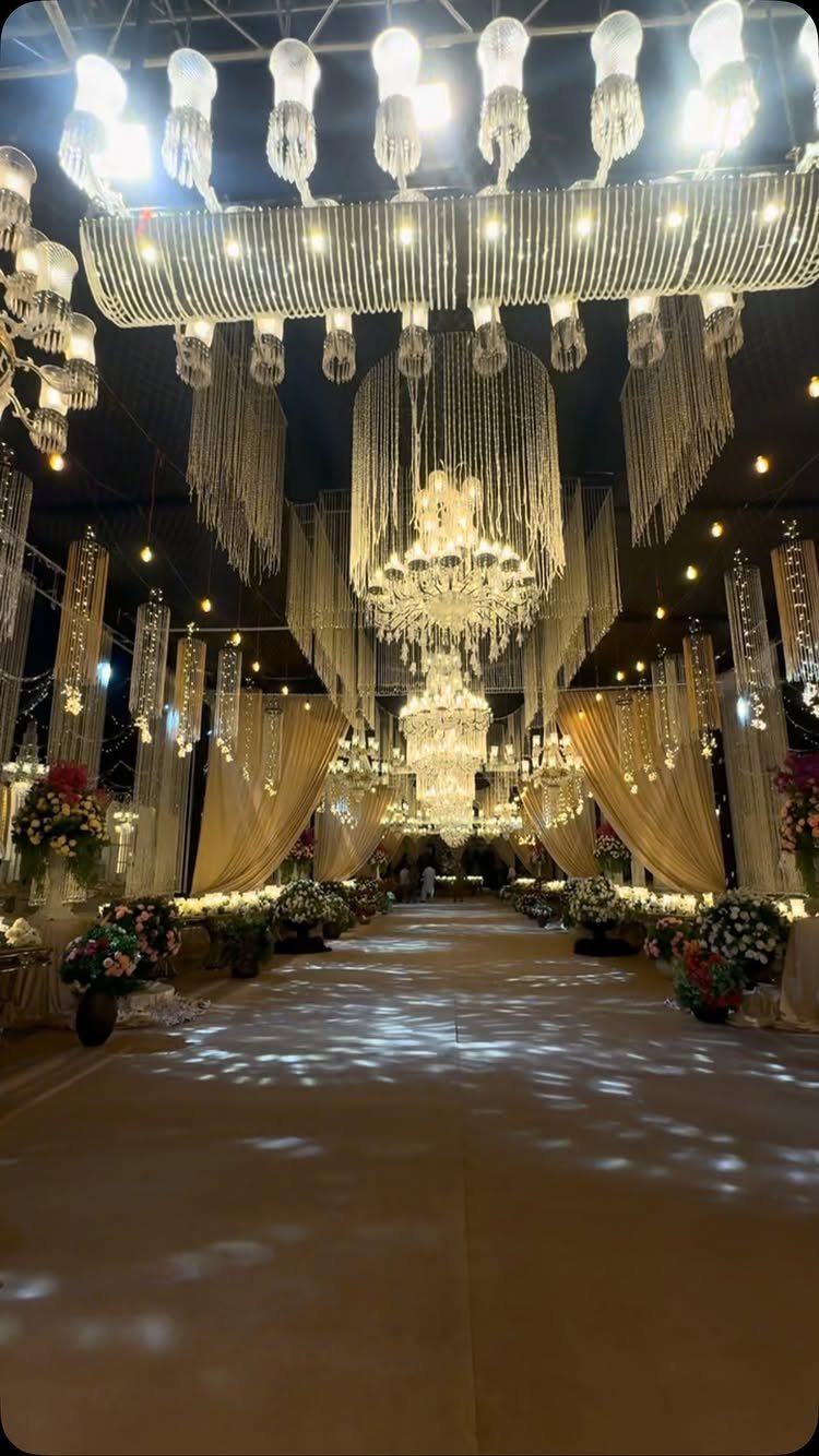 Opulent wedding venue decor with crystal chandeliers, gold drapery, and floral aisle arrangements.