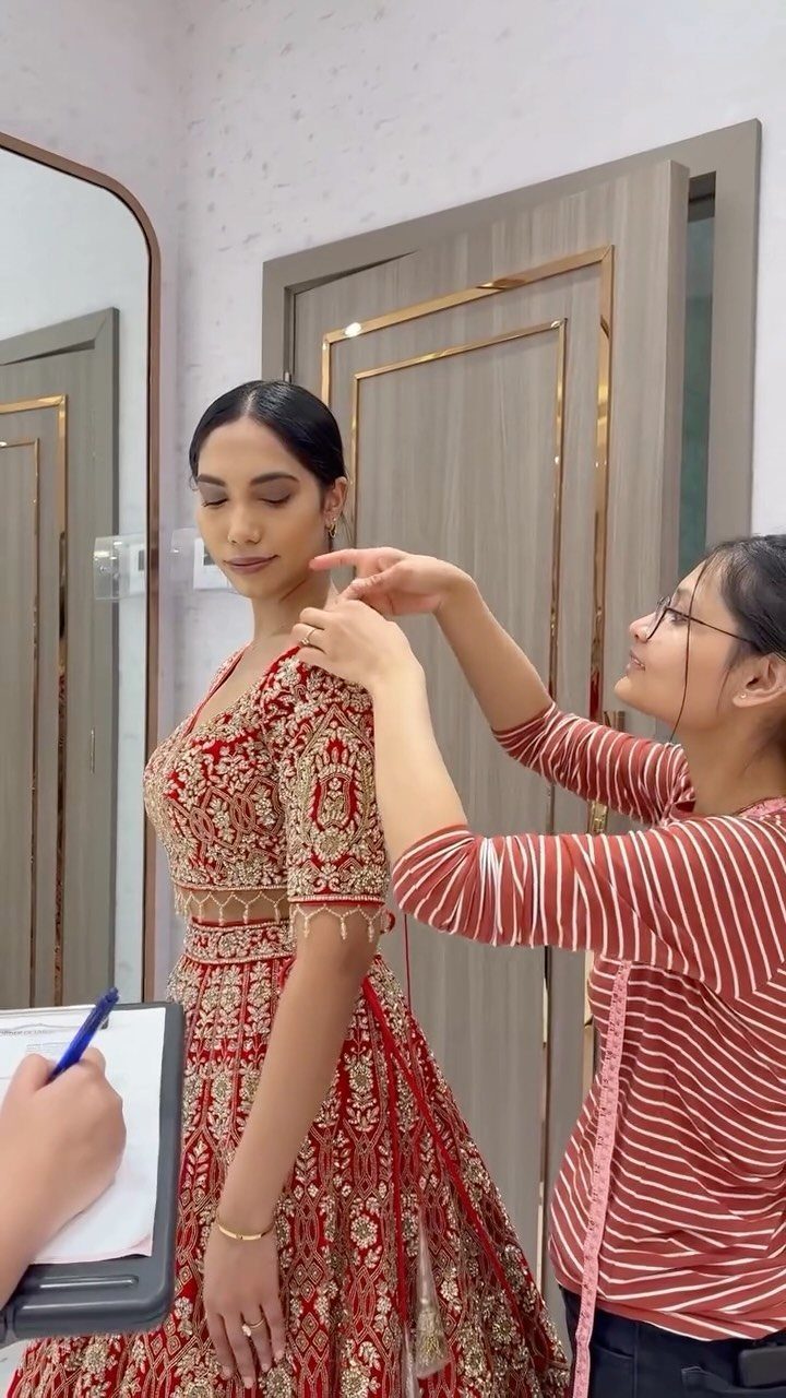 Woman in red bridal lehenga getting a dress fitting from a tailor.