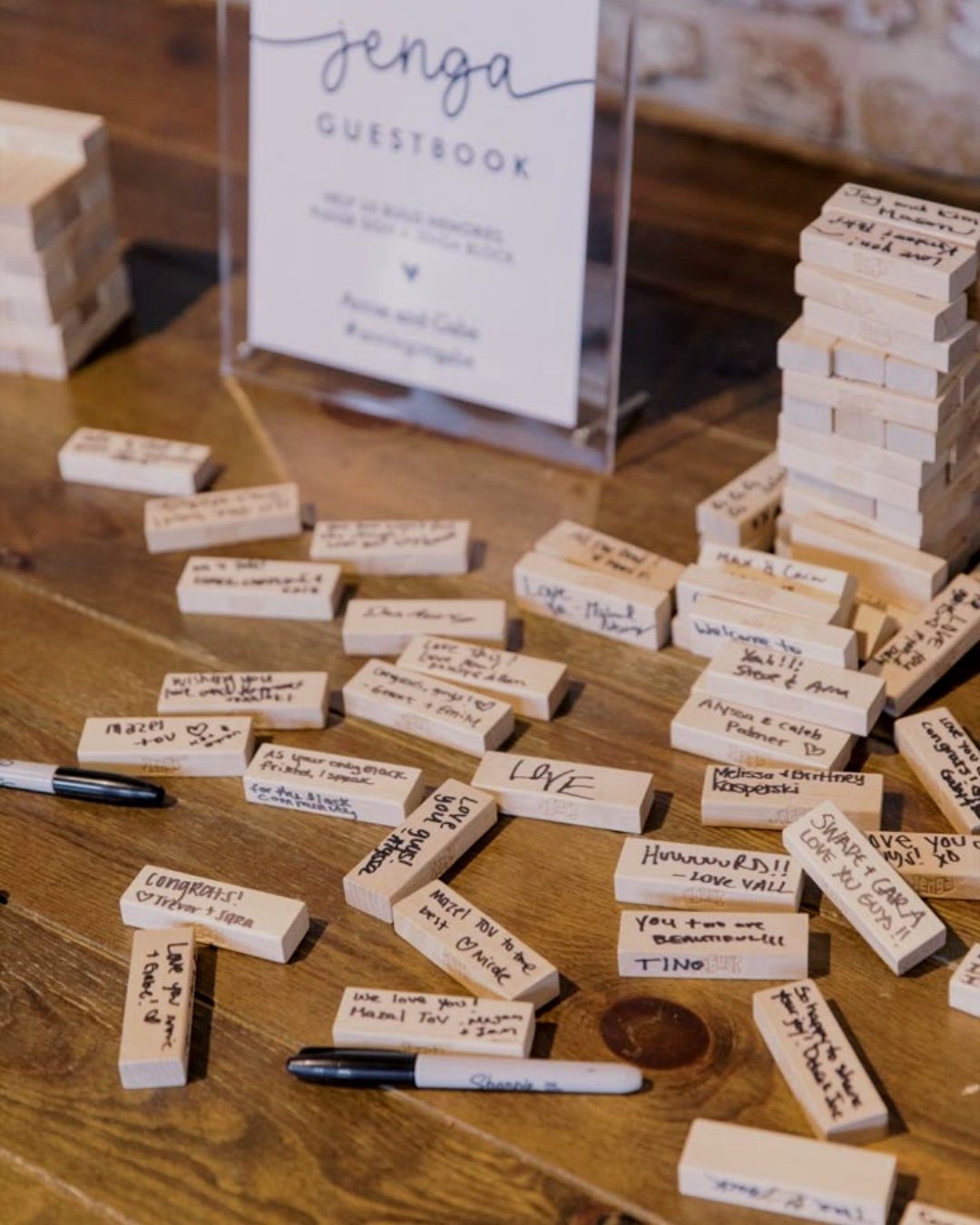 Wooden Jenga blocks with handwritten guest messages and a guestbook sign on a table