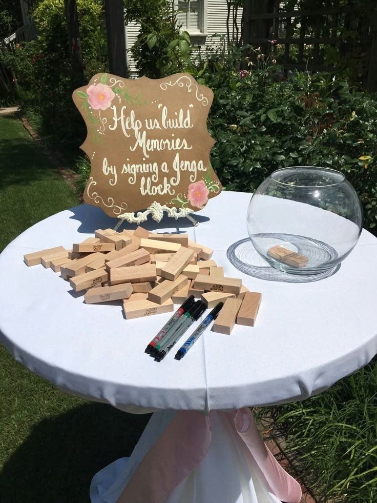 Wooden Jenga blocks and markers on a white table with a guest book sign.