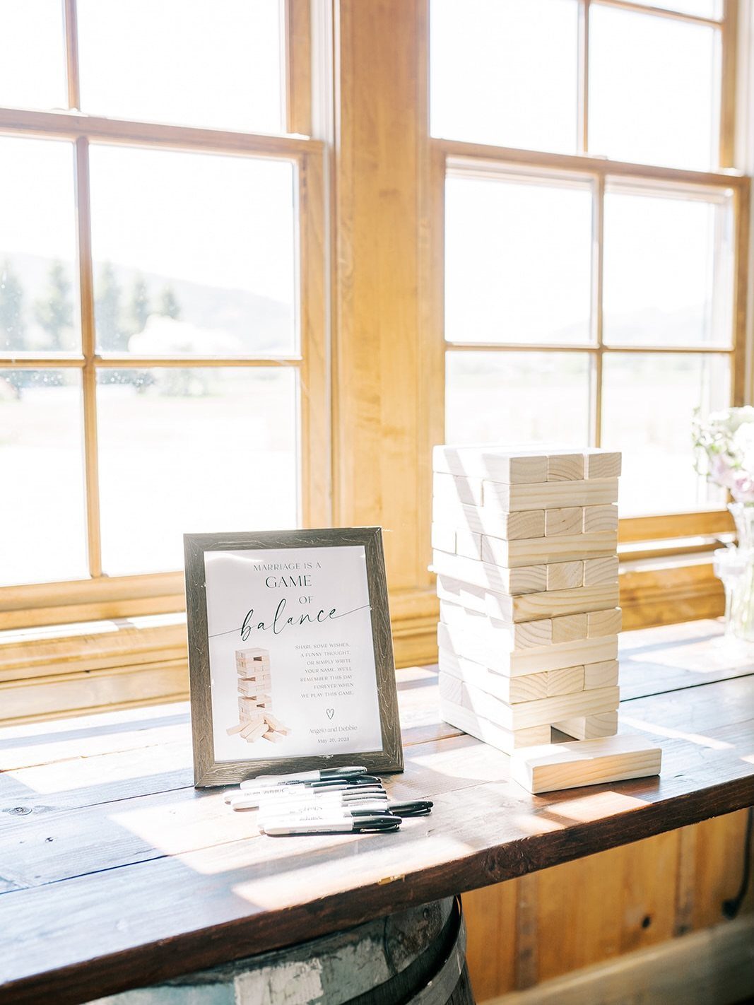 Wooden Jenga block tower and instructional sign on a rustic table by a window
