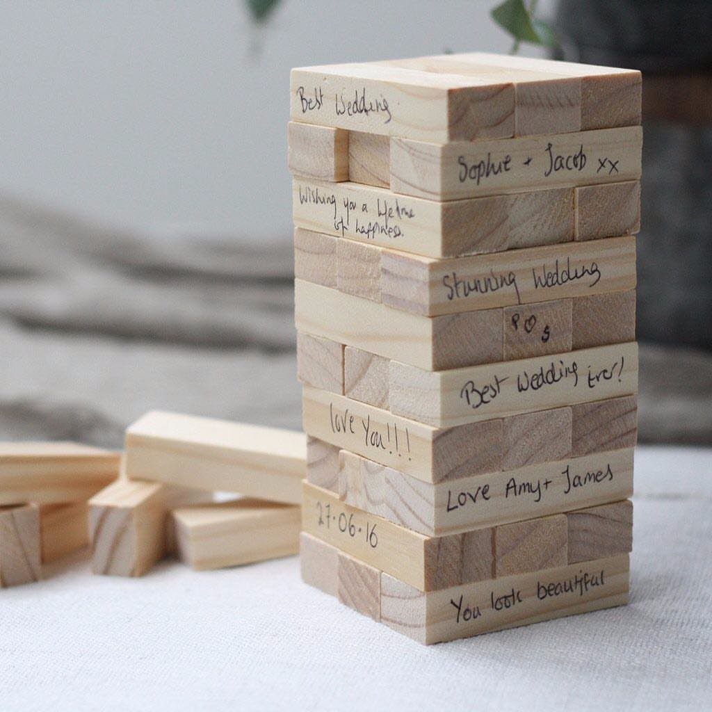 Wooden Jenga blocks stacked with handwritten wedding messages and names on them.