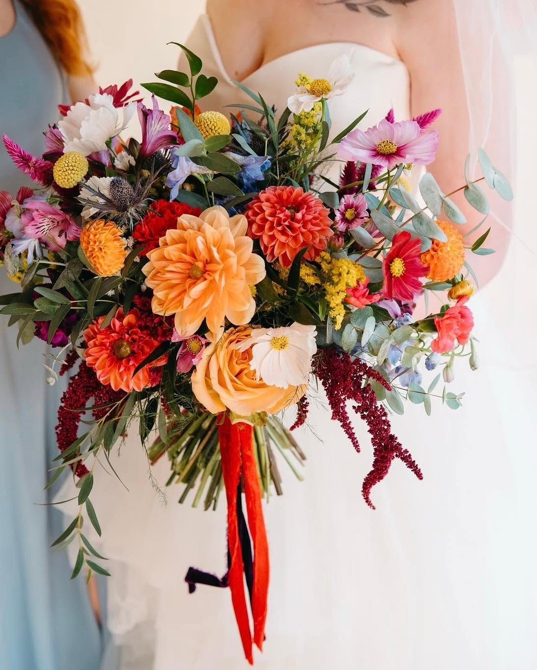 Colorful wedding bouquet with orange dahlias and red flowers held by a bride.