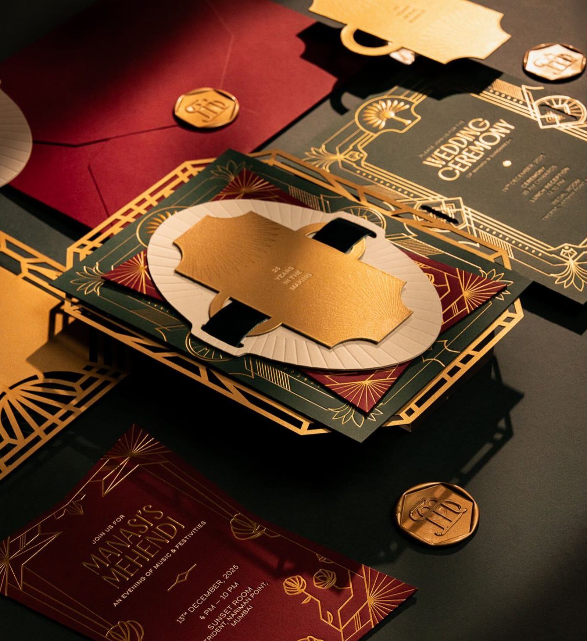 Emerald and burgundy wedding invitations with gold geometric patterns and gold wax seals.