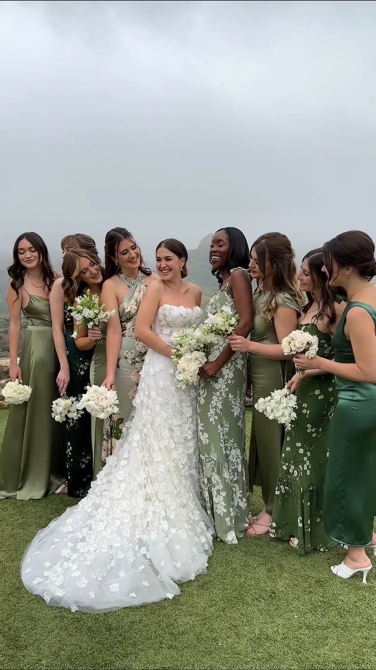 Bride in white lace gown with bridesmaids wearing mismatched green jewel tone dresses.