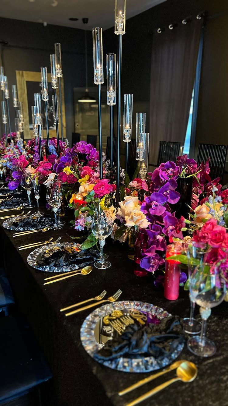 Elegant table setting with black linens, gold cutlery, and vibrant jewel-toned floral arrangements.