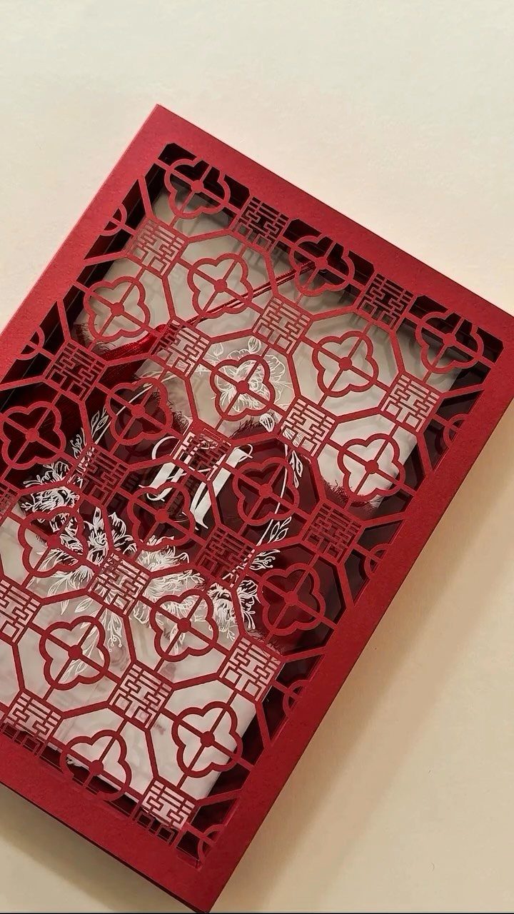 Red laser-cut invitation sleeve with intricate patterns holding a white printed card.