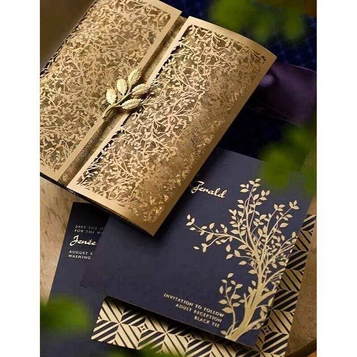 Gold laser-cut floral invitation folder and navy blue card with gold foil lettering.