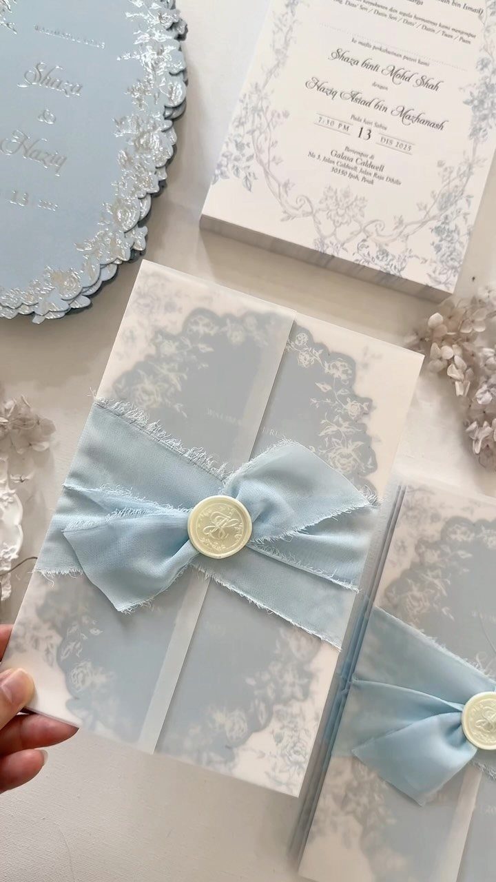 Laser cut wedding invitations in light blue and white with ribbons and wax seals.