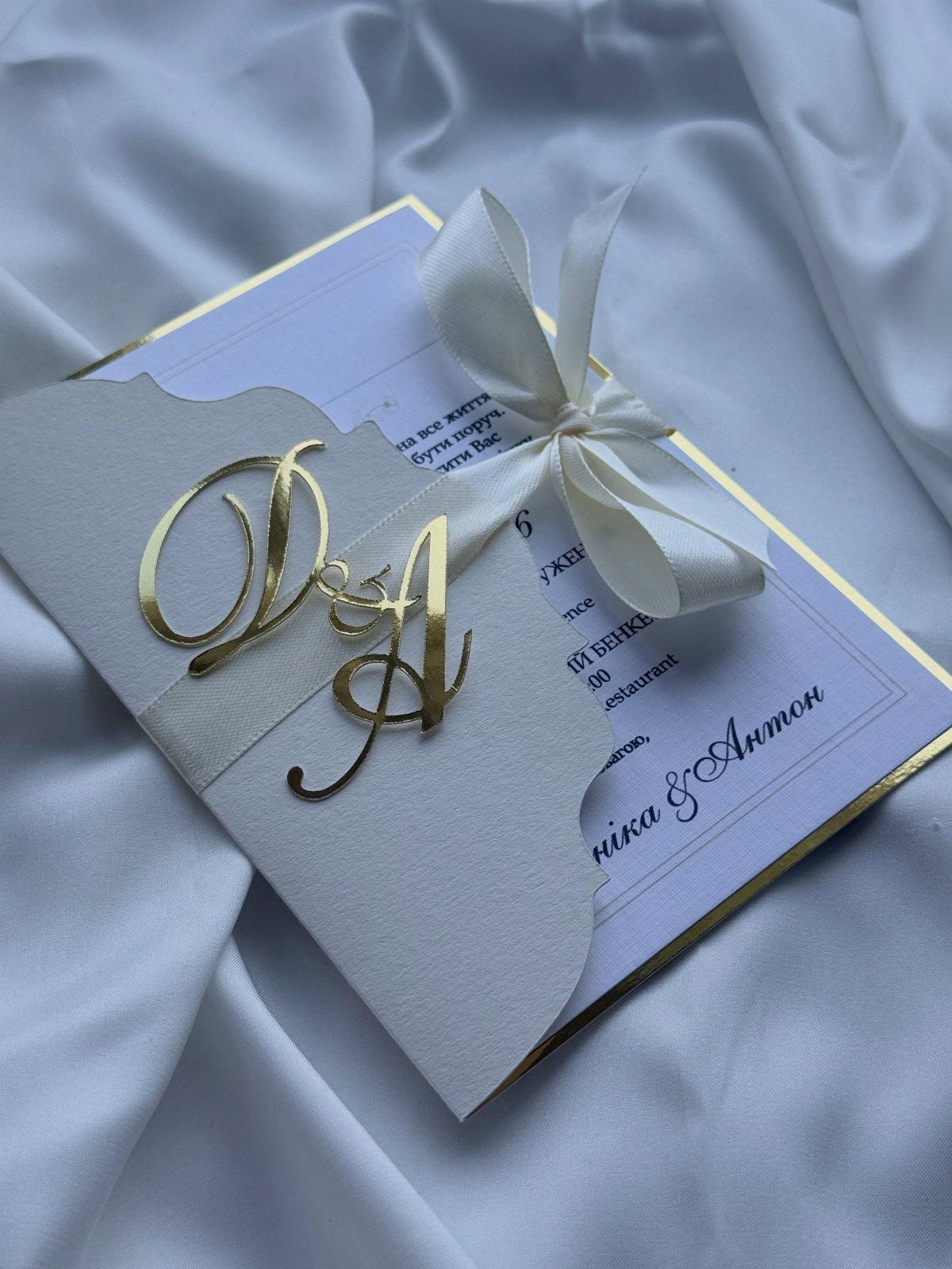 White wedding invitation with gold laser-cut monogram and white ribbon on satin fabric