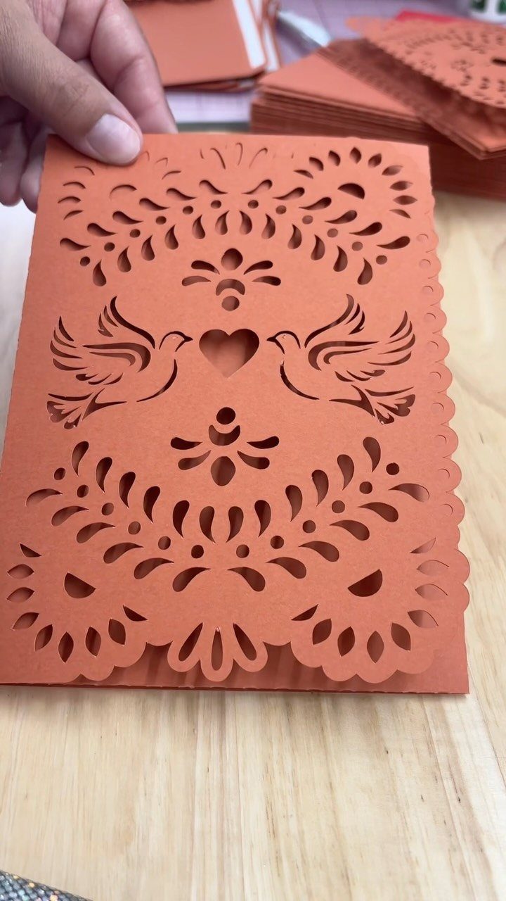 Terracotta laser-cut wedding invitation with bird and heart motifs held by a hand.