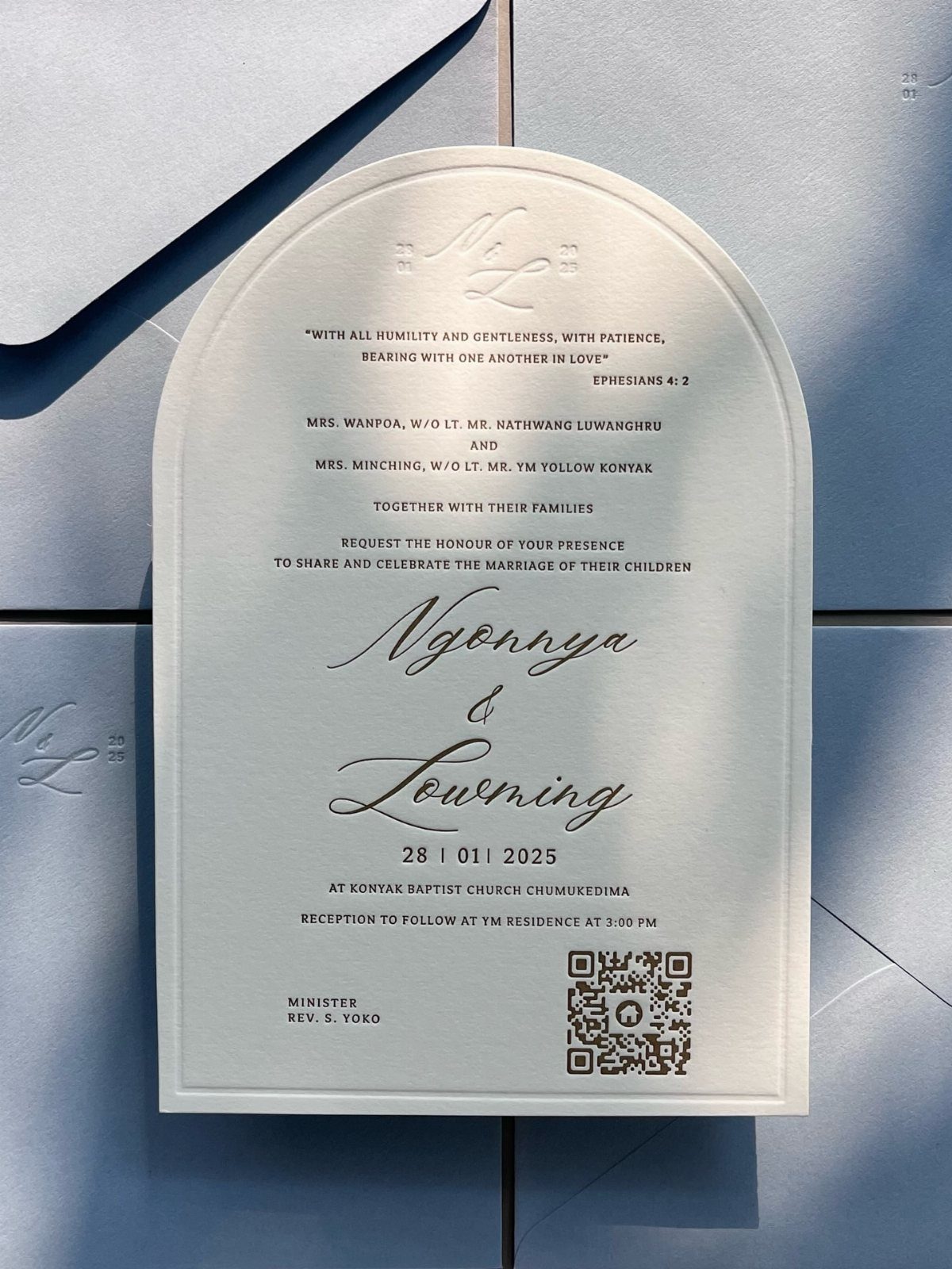 Arched white wedding invitation with black typography on a light blue background