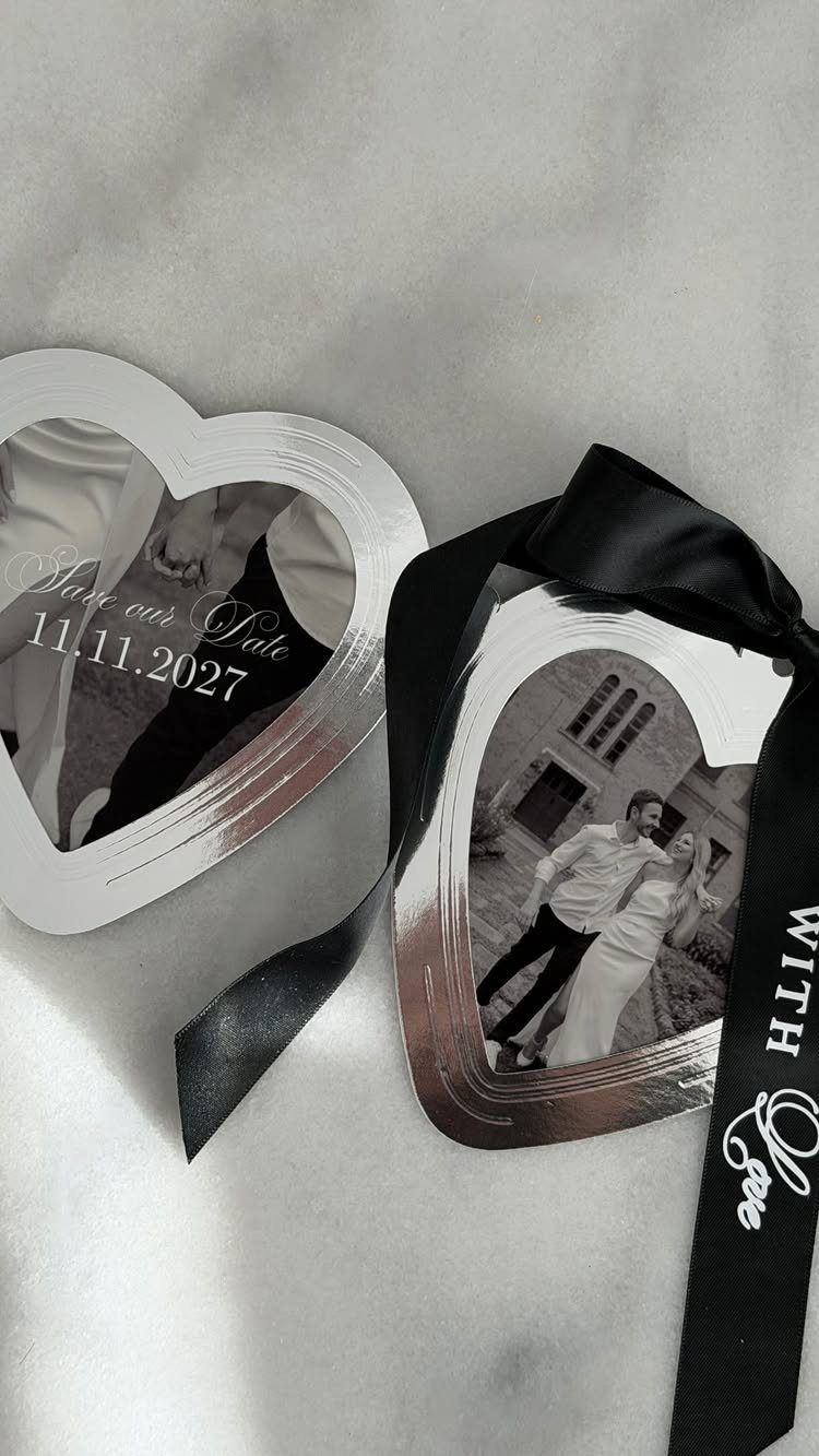 Heart-shaped silver save the date cards with couple photos and a black ribbon.