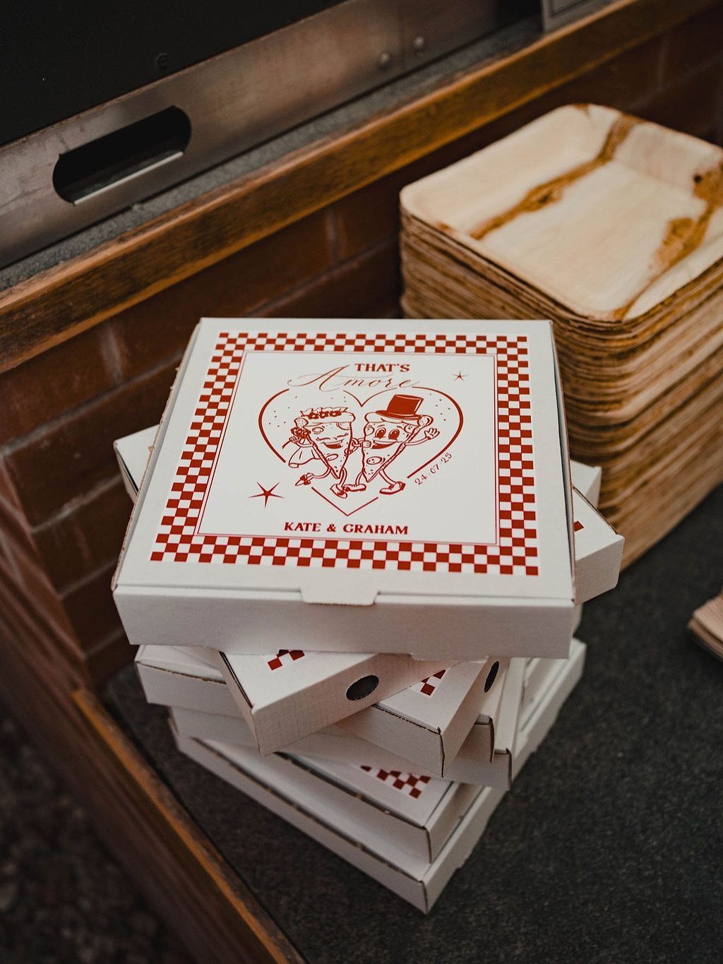 Stacked white pizza boxes with custom red heart illustrations and names for a wedding.