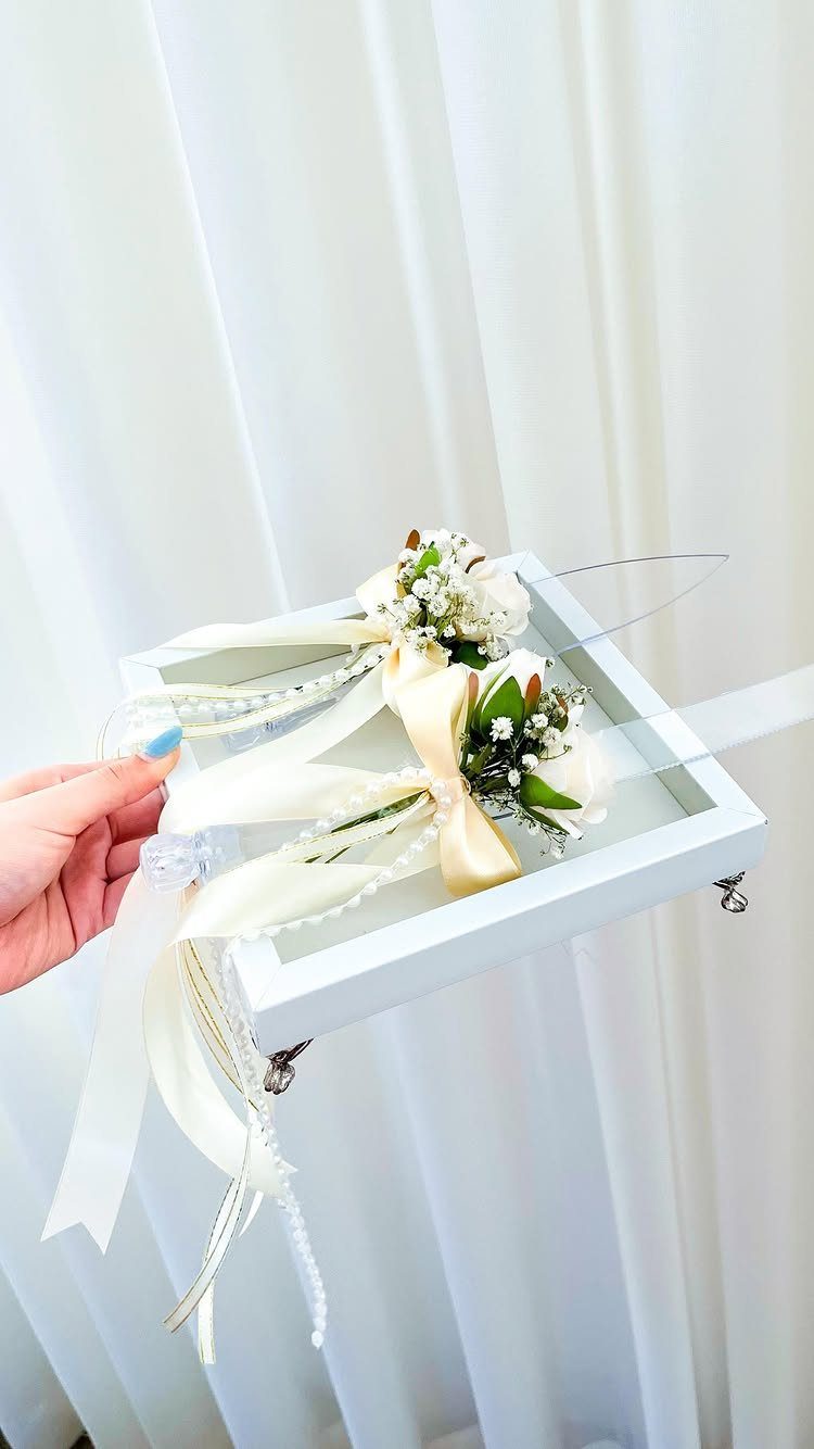 White floral boutonnieres with cream ribbons in a white wooden tray