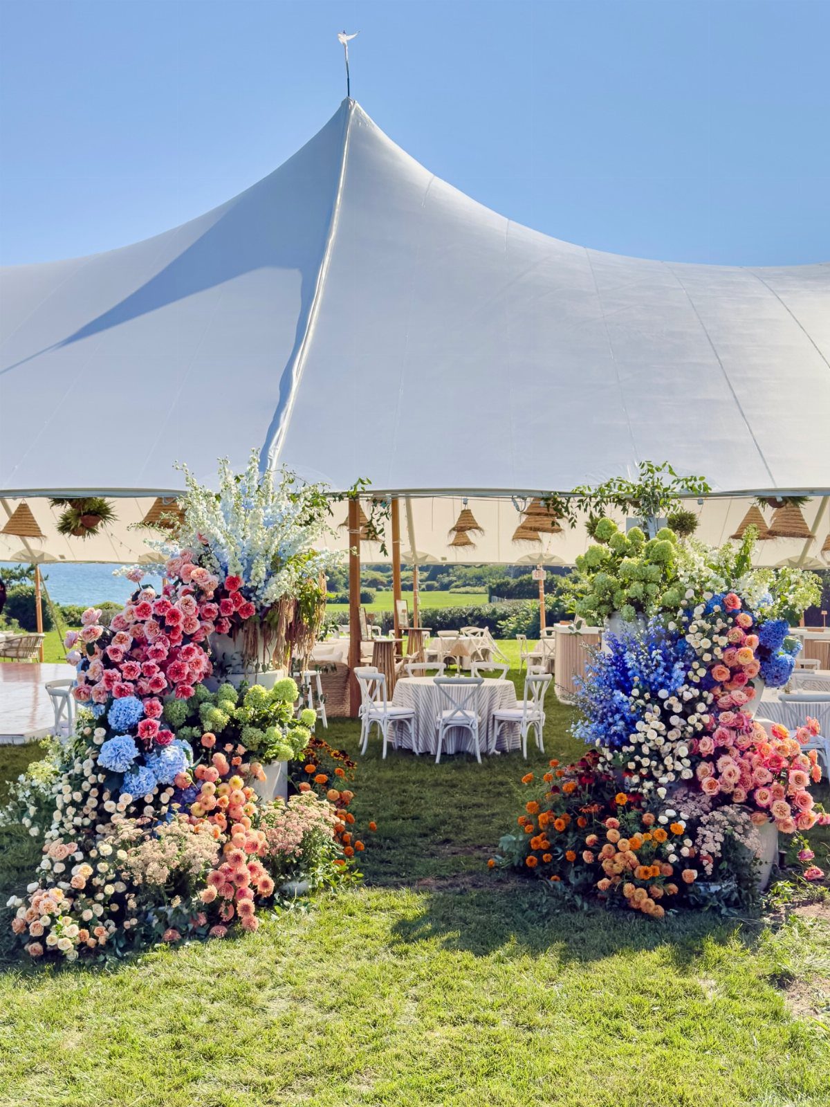 Large white event tent with massive colorful floral arrangements on a green lawn.