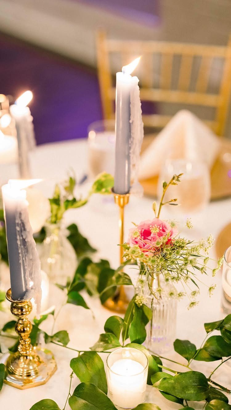 Wedding table centerpiece with grey candles, gold holders, pink flowers, and green vines.