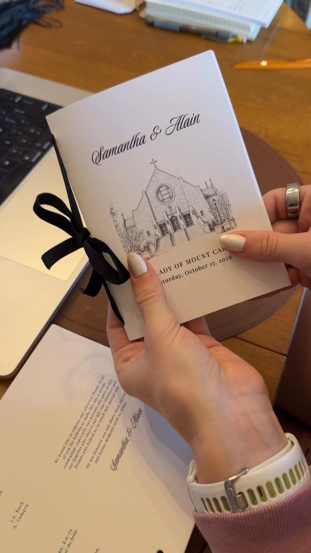 White wedding program with a black ribbon and church illustration held by hands.