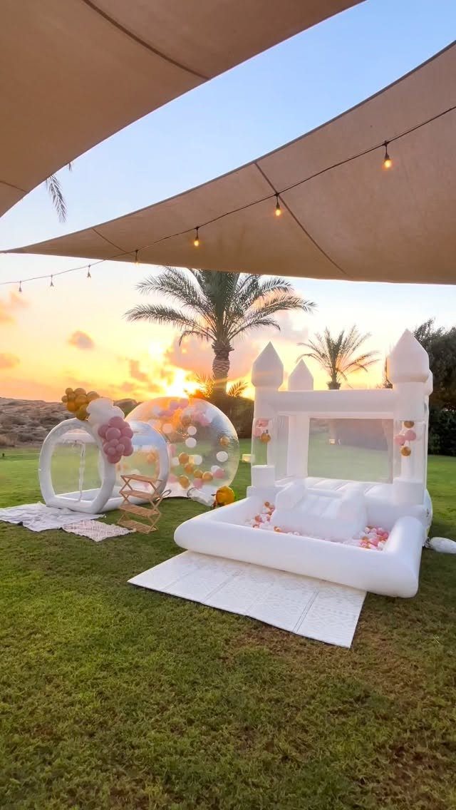 White inflatable castle and bubble tents on a lawn during a sunset wedding.