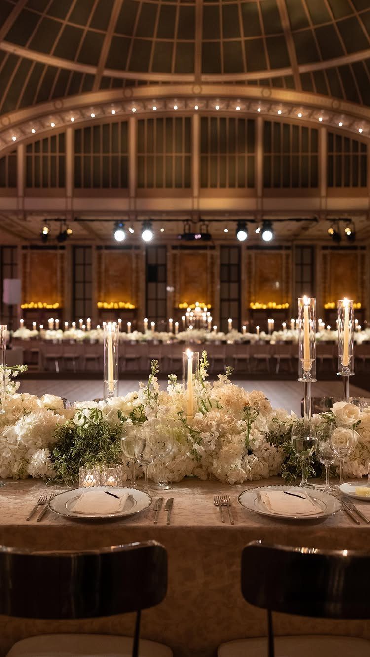 Wedding reception table with white flowers and candles under a grand glass dome.