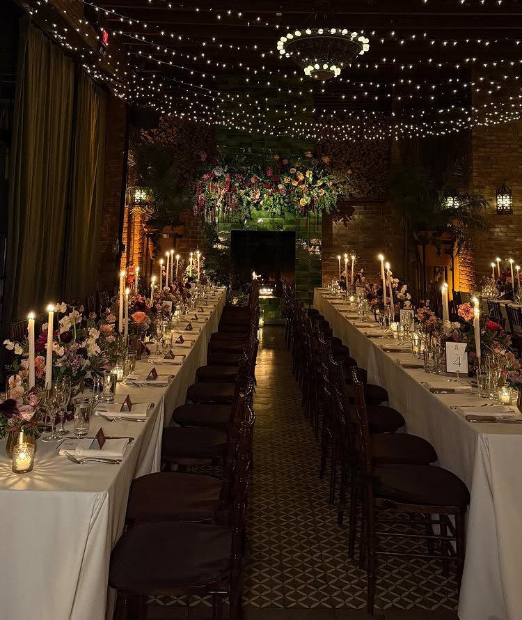 Long wedding tables with candles and floral arrangements under a canopy of fairy lights.